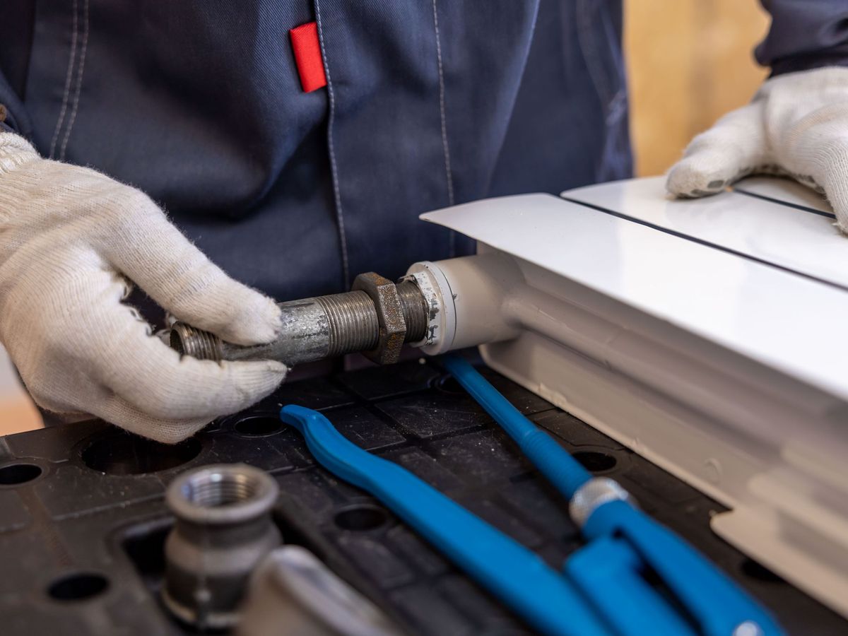 Plumber's gloved hands fitting a pipe with tools